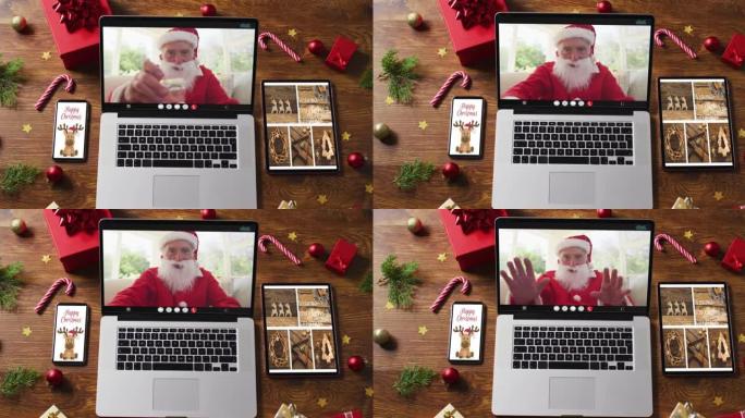 快乐的高级高加索圣诞老人在笔记本电脑上进行视频通话，配有智能手机、平板电脑圣诞装饰品