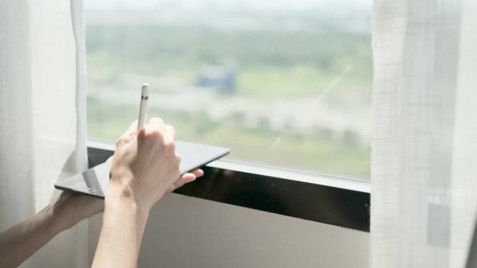 女人的手拿着笔在平板电脑上写字在家窗前，外面和阳光中的4k