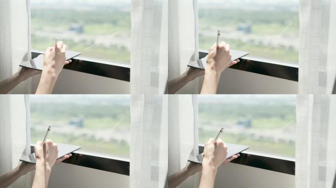 女人的手拿着笔在平板电脑上写字在家窗前，外面和阳光中的4k