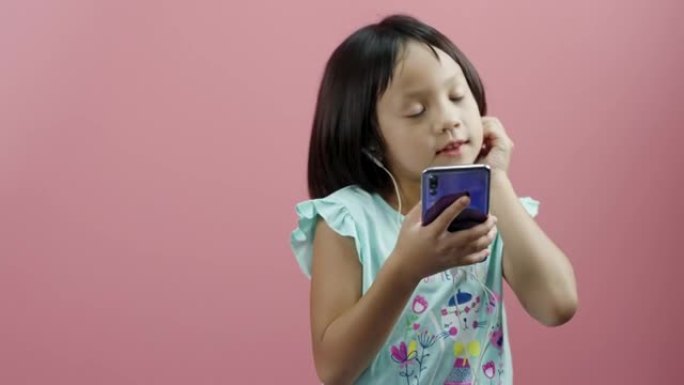 小女孩戴着耳机听音乐，在粉色背景上跳舞。