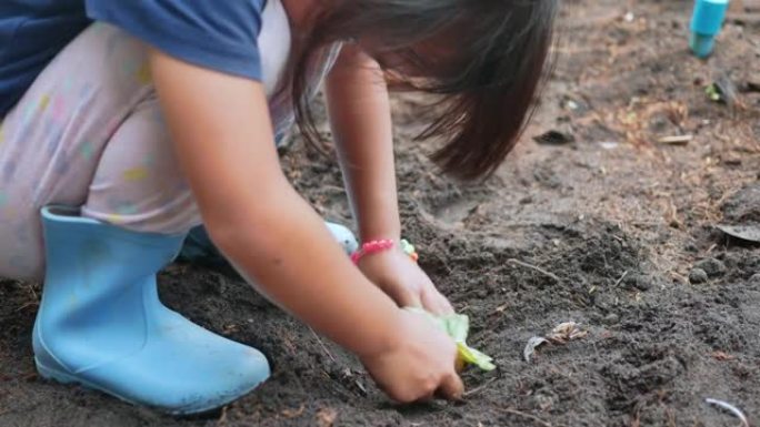 穿着靴子的可爱小女孩在后院种了一棵幼苗。孩子在厨房花园里种菜。