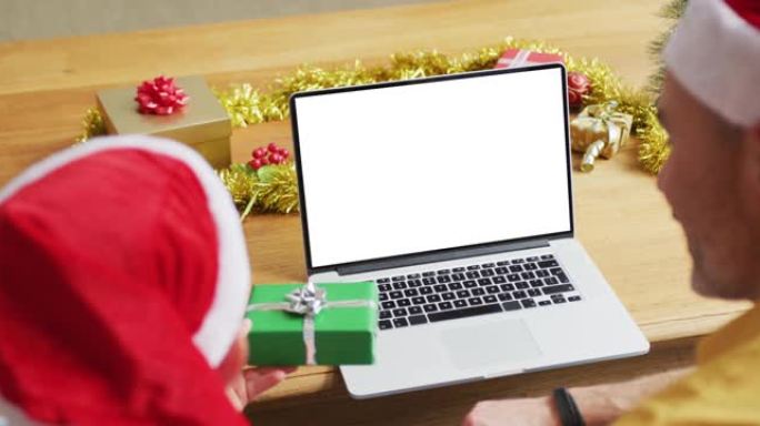 高加索人的父亲和儿子戴着圣诞老人的帽子进行笔记本电脑圣诞节视频通话，在屏幕上复制空间