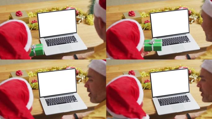 高加索人的父亲和儿子戴着圣诞老人的帽子进行笔记本电脑圣诞节视频通话，在屏幕上复制空间