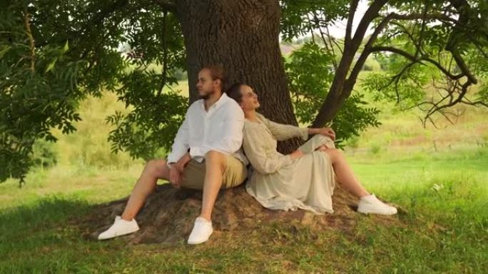 年轻夫妇喜欢在公园的树下背靠背坐着
