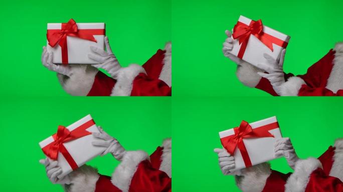 戴着白手套和红色西装的圣诞老人的侧视图在他的手中旋转着一个礼品盒。被隔离在工作室的绿屏上。色度键。特