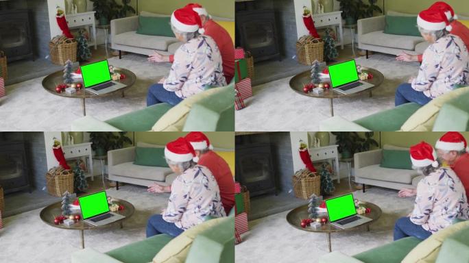 戴着圣诞老人帽子的高级高加索夫妇用绿色屏幕进行笔记本电脑圣诞节视频通话