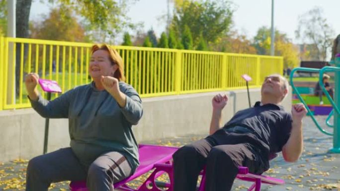 活跃的老年夫妇在户外模拟器上做运动。退休期间，在公园或花园中进行户外运动，以健康和健身。
