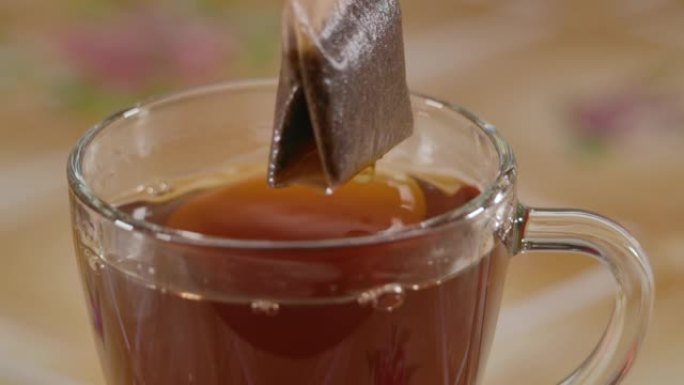 慢动作特写带红茶袋的玻璃杯。做早茶。将茶包放入装满热水的玻璃杯中慢动作特写。