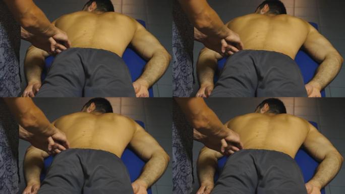 肌肉发达的运动员躺在按摩台上，专业按摩师的手臂在沙龙里按摩他的腰。按摩师训练后放松和振兴运动员的肌肉