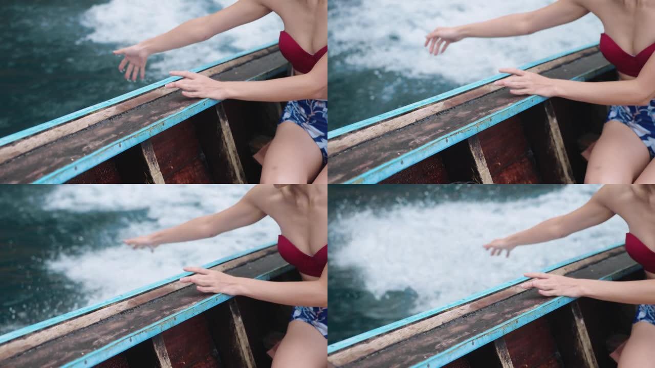 年轻女子穿着比基尼享受岛屿之旅，坐在热带长尾船上，伸手到水，玩水飞溅，起航到海洋，暑假