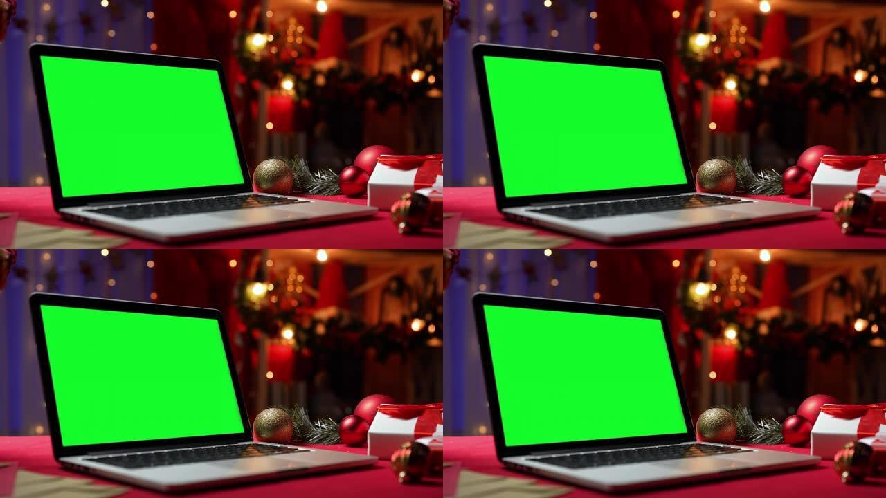 带有绿屏色度键的打开笔记本电脑站在礼物和玩具旁边的红色桌子上。家庭房间，圣诞装饰和灯光在模糊的背景。