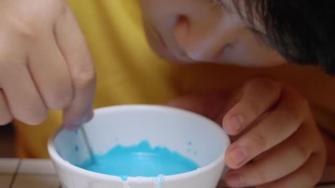 亚洲男孩在糖糖碗中混合蓝色，用于装饰万圣节饼干，生活方式概念。