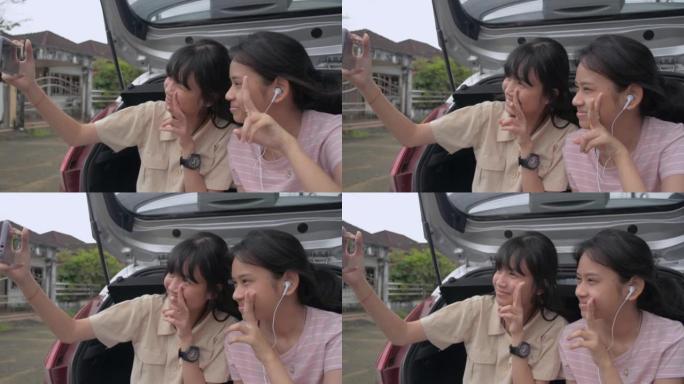 两个泰国可爱的少女姐妹坐在掀背车的后侧，喜欢用手机拍照。年轻的生活方式。