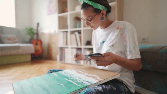 现代年轻女子，一位艺术家尝试一种新的绘画风格，同时在手机上遵循绘画教程