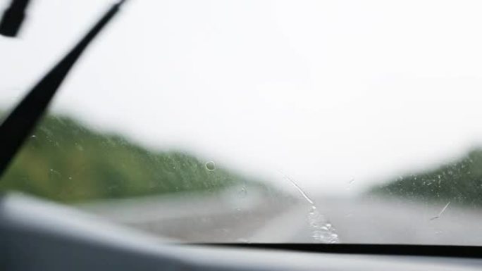 在能见度有限的条件下驾驶汽车: 大雨，刮水器清洁挡风玻璃。高速公路上有大灯的迎面而来的交通。恶劣天气