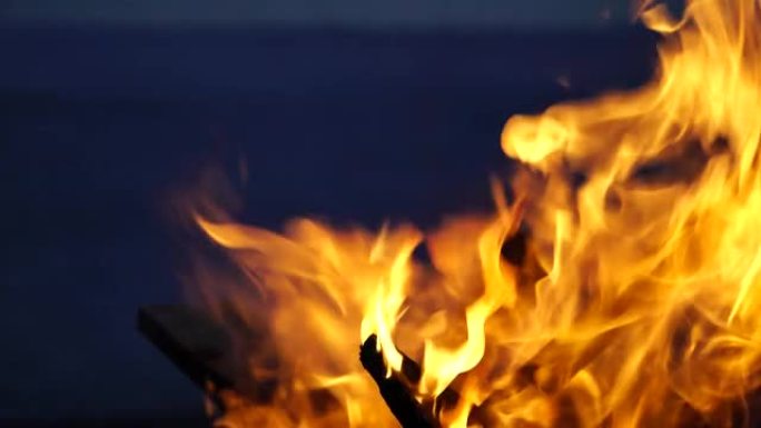 火盆烧烤烧烤炉中鲜红色的大火特写镜头。明亮的篝火，充满活力的灯光，灰烬，烟雾，并在日落之后平静的大海