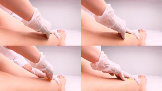 裁切的视频美容师双手戴着医用手套，用shugaring对女人的腿进行脱毛。舒加酱