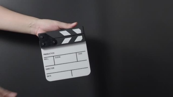 电影石板或拍板。近距离握着空的胶片石板，并在黑色背景上鼓掌。用于视频制作的打开和关闭胶片板。电影制作