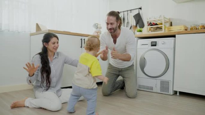 白人热爱的父母在厨房的地板上与男婴玩耍。幸福的家庭，迷人的美丽年轻夫妇爸爸和妈妈跳舞可爱的婴儿蹒跚学