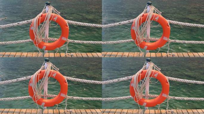橙色的生命线和海绳在海和蓝天的背景。挂在柱子上的海洋绳索和救生圈。帮助和安全概念