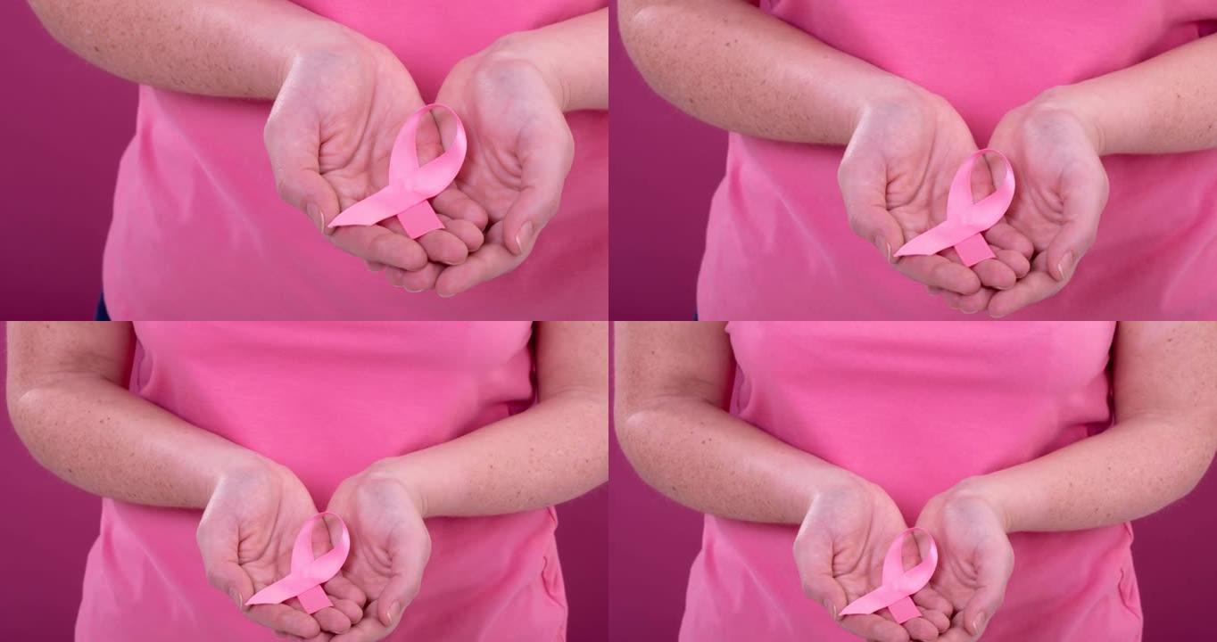 白人妇女手持粉红色癌症意识彩带，背景为粉红色
