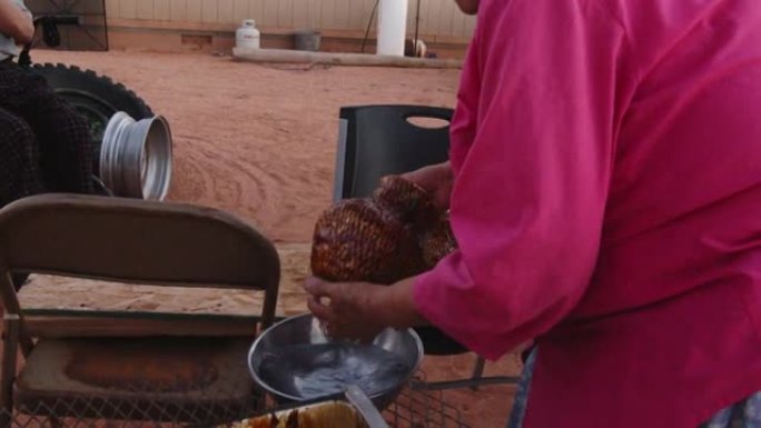 纳瓦霍 (Navajo) 老年妇女在新编织的篮子上涂上沥青，在室外的柴火炉上加热，她的丈夫和孙子看着