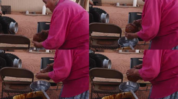 纳瓦霍 (Navajo) 老年妇女在新编织的篮子上涂上沥青，在室外的柴火炉上加热，她的丈夫和孙子看着
