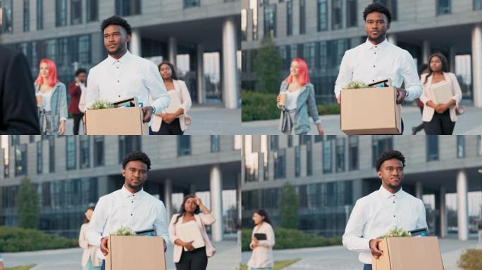一个皮肤黝黑的长期上班族被解雇，与同事一起走出公司大楼，手里拿着一盒包装好的物品，不满的表情，愤怒，