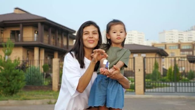 年轻女子和亚洲小女孩展示新公寓的钥匙