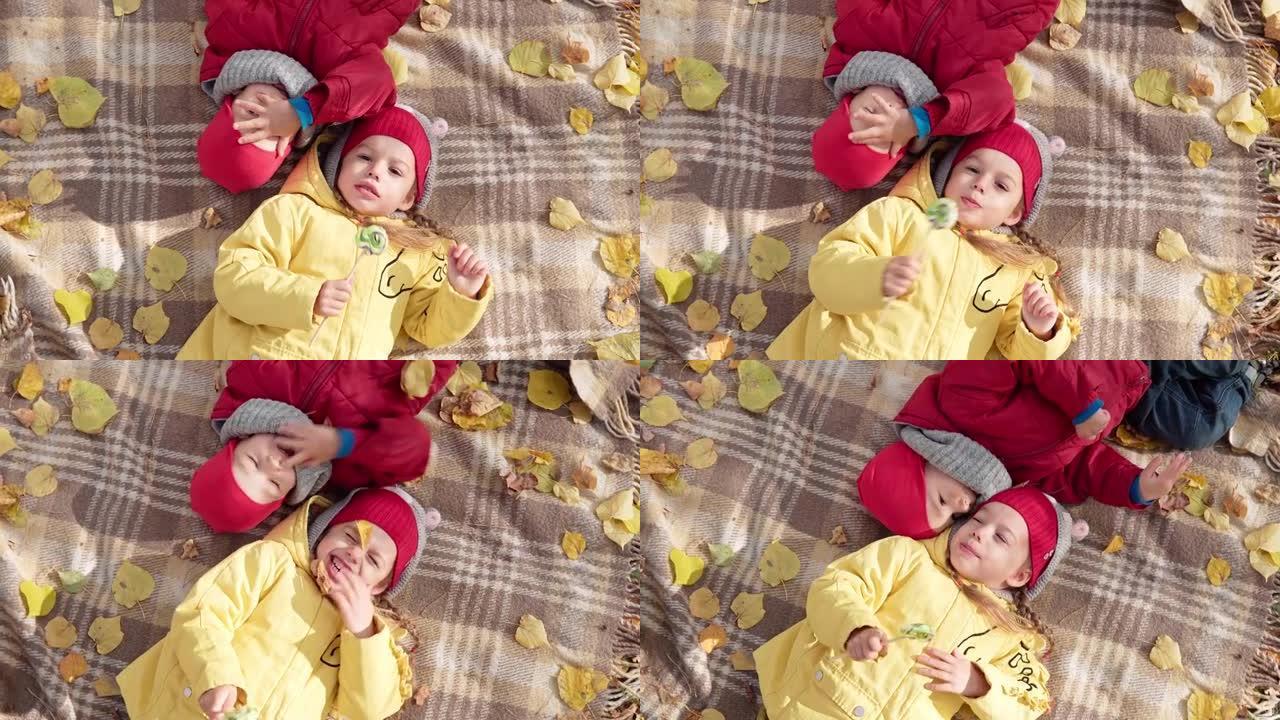 学龄前儿童兄弟姐妹女孩男孩微笑着躺在篮子里的格子落叶上休息放松野餐儿童在秋天公园吃糖果糖果看相机。家
