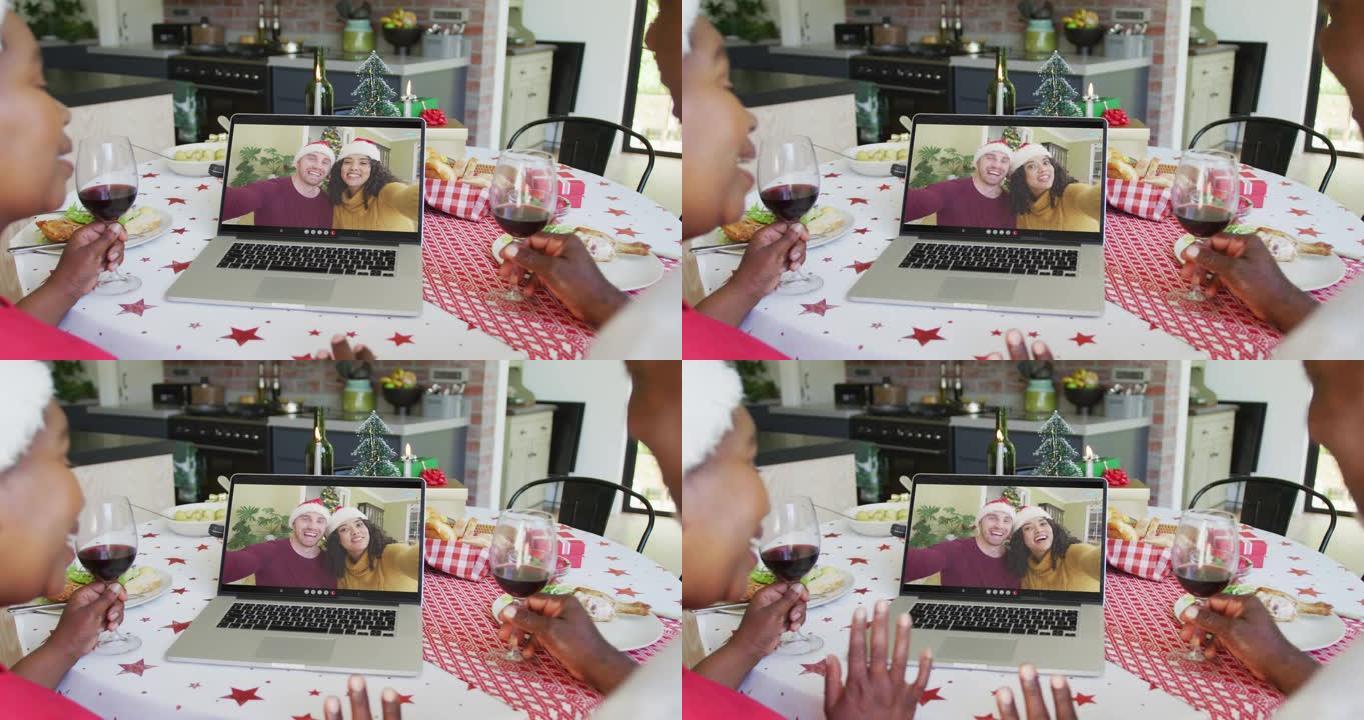 非裔美国人夫妇与葡萄酒使用笔记本电脑进行圣诞节视频通话与夫妇在屏幕上