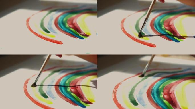 小女孩手里拿着刷子，用彩色颜料在白纸上画彩虹。微距拍摄