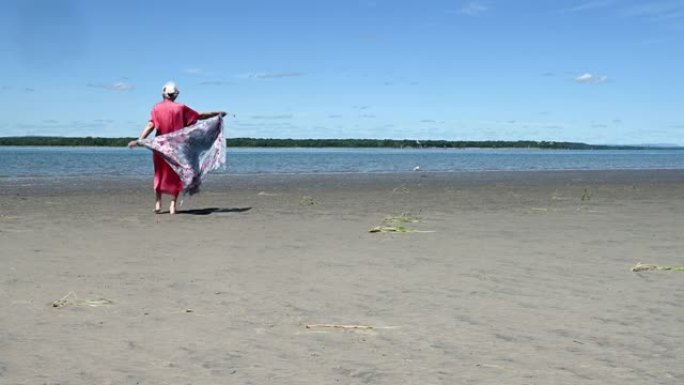 老年妇女独自在夏季海滩放松散步