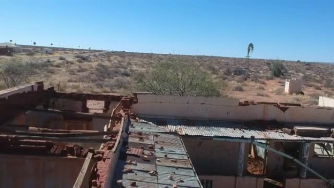 俯视门廊和摄像机，从半干旱景观上的一栋废弃建筑的屋顶上向上移动，一条通往远处的道路航拍视频