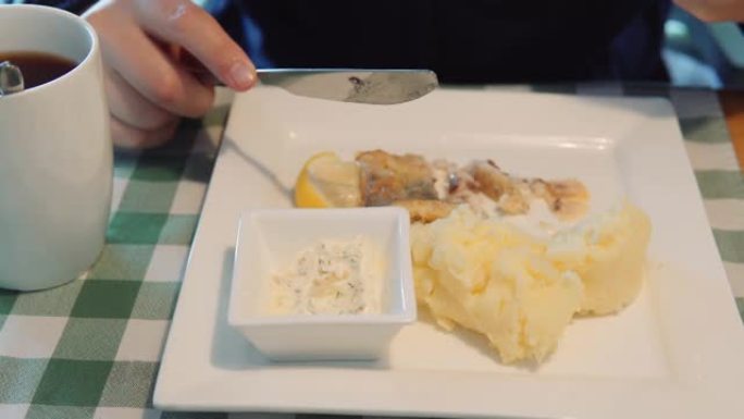 一名男子坐在餐馆里用刀叉吃自制的鱼和土豆泥配鞑靼酱