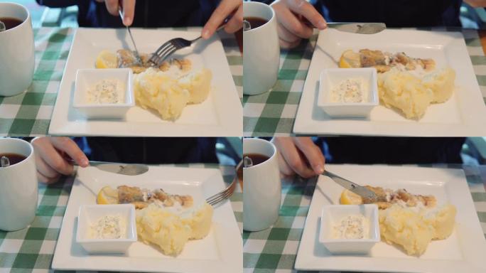 一名男子坐在餐馆里用刀叉吃自制的鱼和土豆泥配鞑靼酱