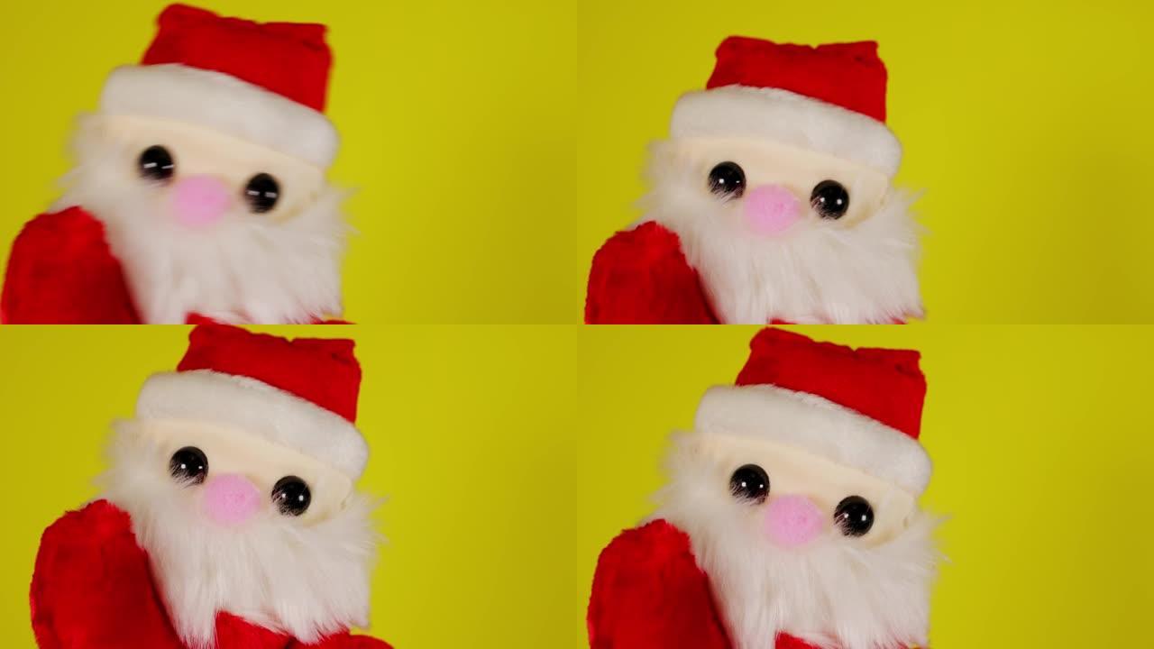 黄色背景上圣诞老人的毛绒玩具。手边圣诞老人木偶的特写。布袋戏的概念和即将到来的新年假期