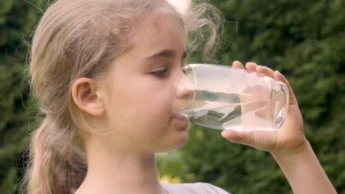 口渴的孩子在户外用玻璃喝水，阳光普照。可爱女孩水杯新鲜透明纯净水慢动作儿童水杯水健康身体护理健康生活
