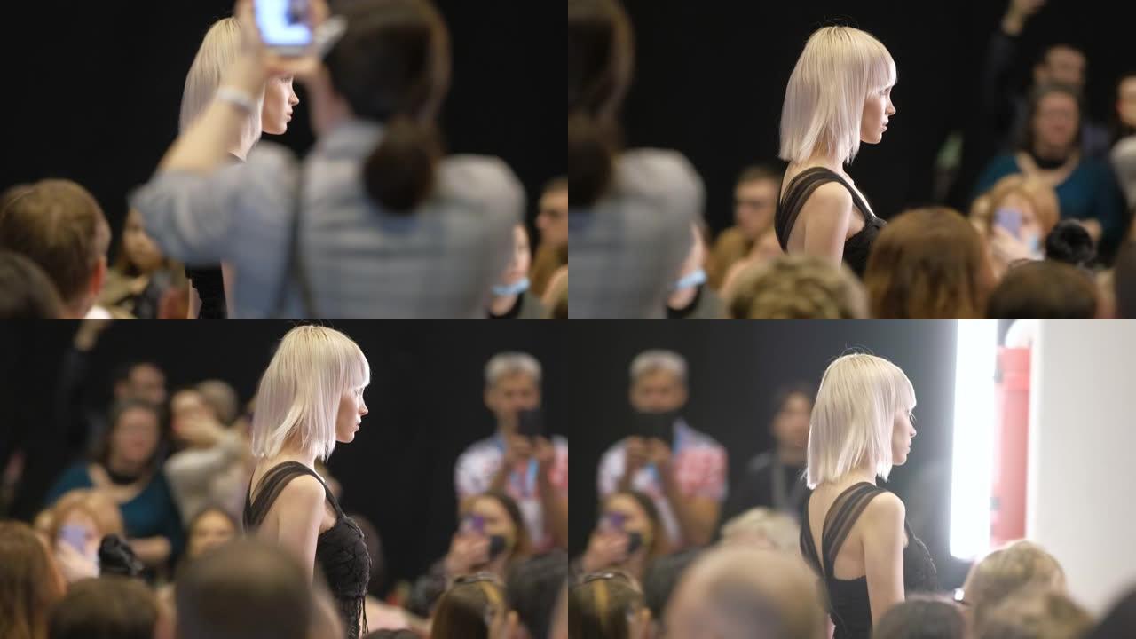 灰白发的女孩在t台走秀讲台上移动。模特女人玷污
