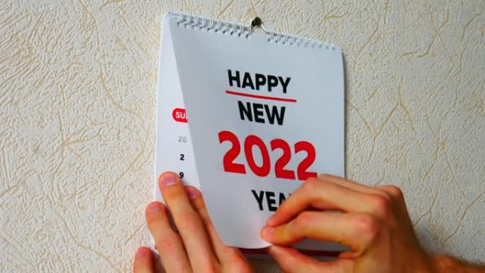 一个男人的手撕下墙上2022日历的标题页的特写，然后是1月页