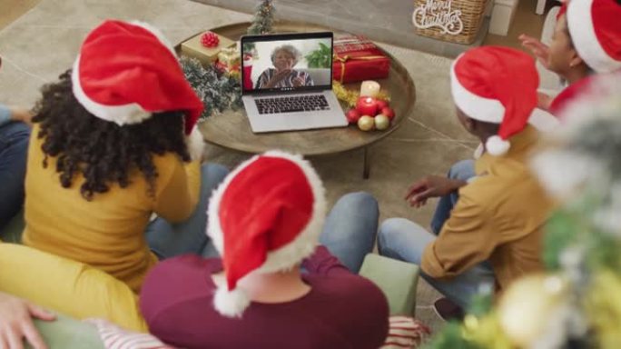 拥有圣诞老人帽子的多元化家庭使用笔记本电脑进行圣诞节视频通话，屏幕上有微笑的女人