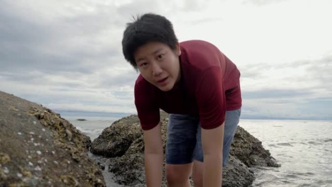 快乐的亚洲男孩在大海的岩石上寻找和捕捉平静，生活方式的概念。