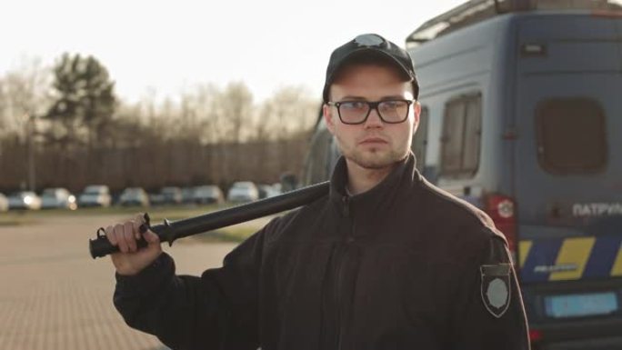 一名身穿警服的男子正转过头，认真地看着镜头。他肩上扛着警棍。背景中有两辆警车。4K