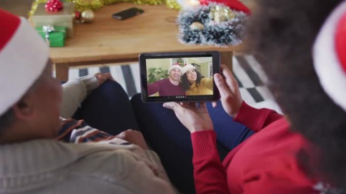非裔美国母亲和女儿使用平板电脑进行圣诞节视频通话，屏幕上有情侣