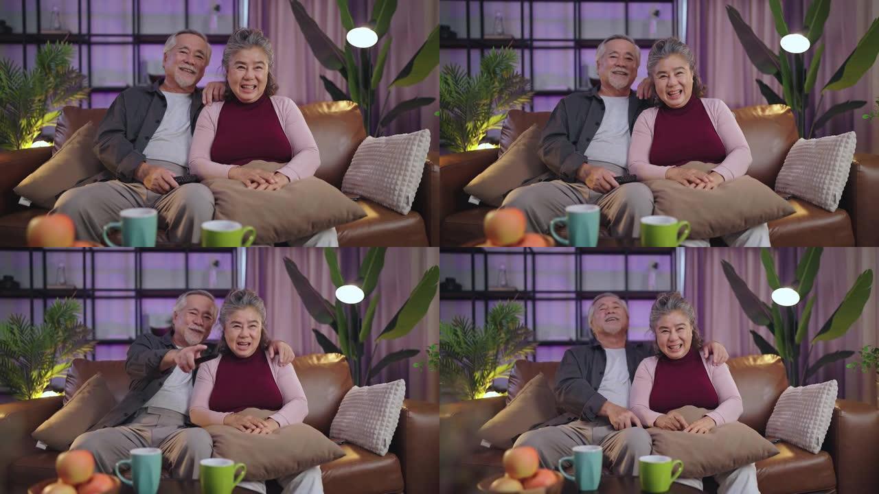 老年退休亚洲夫妇在家看电视，老年成熟亚洲夫妇欢呼体育比赛与笑笑胜利沙发沙发在客厅家庭隔离活动