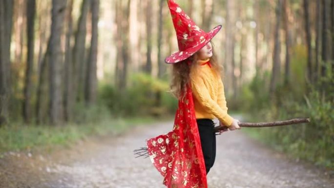 一个穿着女巫服装，戴着扫帚的帽子的女孩在秋天的森林里玩耍，参加万圣节派对