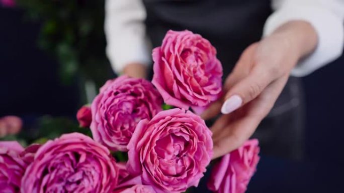 花店的手抚摸和触摸粉红玫瑰的特写镜头。花店在工作室里为花束准备鲜花