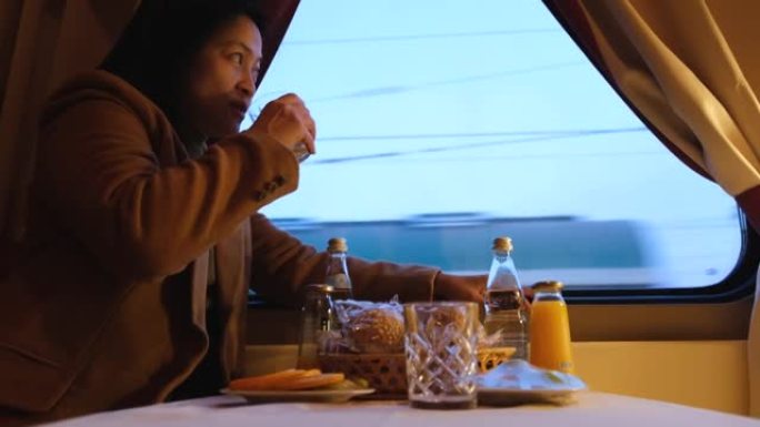 穿着棕色外套的亚洲女人吃早餐，独自乘火车旅行，透过窗户看风景