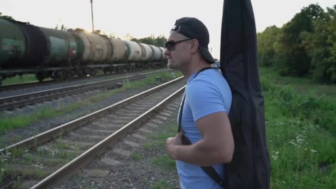 戴着墨镜的男人和吉他盒站在铁路道口