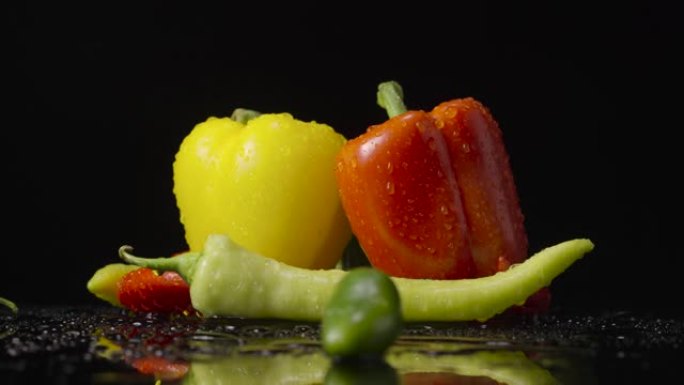 黑色背景上滴着湿气的胡椒。红色，绿色和黄色的辣椒，墨西哥胡椒和甜椒被水滴覆盖。特写。慢动作就绪，4k